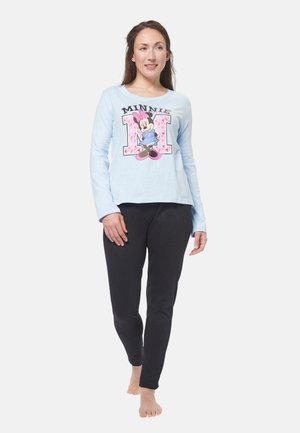 Camicetta a maniche lunghe di colore azzurro chiaro con una grafica di un personaggio e la scritta "MINNIE"; abbinata a pantaloni neri attillati. I piedi sono scalzi.