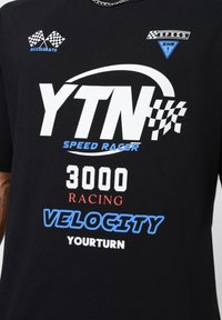 Sort t-shirt med et hvidt og blåt grafisk print med teksten: "YTN SPEED RAGER 3000 RACING VELOCITY YOURTURN" og racerløbsflag.
