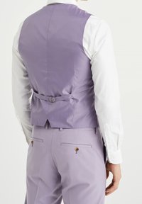 Fialová vesta s hladkou texturou, detailem přezky na zádech a bílou košilí pod ní. Kalhoty jsou fialové s kapsami na zádech na knoflíky.