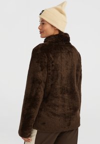 Brun plys fleece jakke med høj krave og blød tekstur. Stylet med en beige strikket hue. Simpelt design, ingen synlige metaldele.