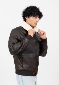 Bruine leren jack met een crèmekleurige nep-shearling kraag, een ritssluiting aan de voorkant en twee klepzakken met geribde manchetten en zoom.