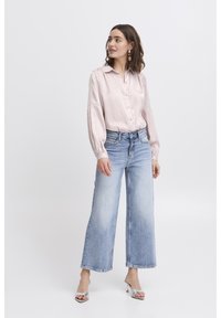 Light pink, button-up blouse with long, billowy sleeves paired with light blue, wide-leg jeans. Accessorized with silver heeled sandals.