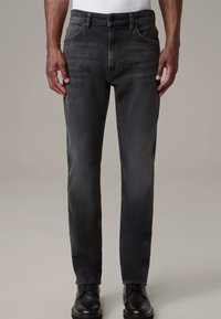 Jeans grises con un corte entallado, fabricados en denim. Presentan un diseño clásico de cinco bolsillos y un cierre de botón. Combinados con zapatos de vestir negros.