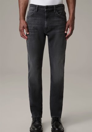 Jeans grises con un corte entallado, fabricados en denim. Presentan un diseño clásico de cinco bolsillos y un cierre de botón. Combinados con zapatos de vestir negros.