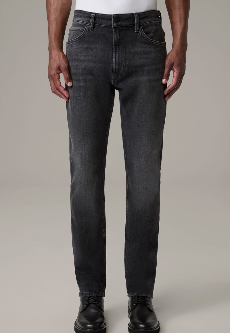 Jeans grises con un corte entallado, fabricados en denim. Presentan un diseño clásico de cinco bolsillos y un cierre de botón. Combinados con zapatos de vestir negros.