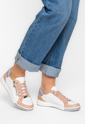 Person wearing rolled-up blue jeans and white sneakers with beige and light purple accents, standing against a white background.