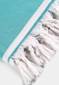 Turkusowo-biała tkanina o splocie jodełkowym, z białymi frędzlami na krawędzi i gładką fakturą.