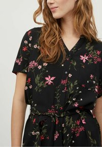 Sort skjortekjole med korte ærmer, der har flerfarvede blomsterprint, knapper foran og et bindebælte i taljen for justerbar pasform.