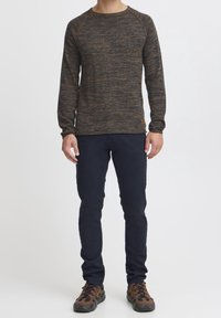 Dunkel meliertes Strickpullover mit langen Ärmeln, rundem Halsausschnitt und gerippten Bündchen; kombiniert mit dunklen Hosen und braunen, mehrfarbig strukturierten Schuhen.