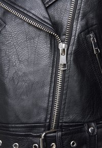 Giacca da biker in pelle nera con finitura testurizzata, accessori in argento, cerniera diagonale e vita con cintura e borchie metalliche.