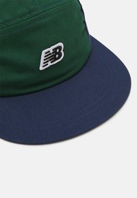 Sombrero de cubo verde y marino con ala plana. Cuenta con un logo bordado en blanco que dice "NB". Está hecho de un tejido suave y duradero con costuras visibles.