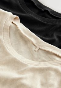 Trzy warstwowe t-shirty z ribbingu w kolorze czarnym i beżowym, z okrągłymi dekoltami i widocznymi detalami szwów. Miękka, teksturowana tkanina.