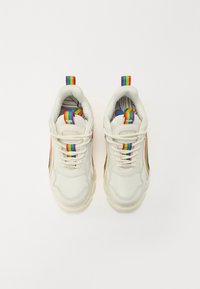 Fehér sneaker, szivárványcsíkkal díszített húzófülekkel és részletekkel, textúrált hálós és szintetikus felsőrésszel, vastag gumitalppal és grafikával ellátott talpbetéttel.