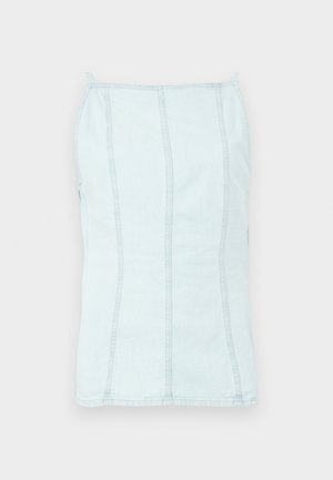 Kobieta modelka o ciemnych włosach, ubrana w jasnoniebieski bezrękawnik, białe spodnie z szerokimi nogawkami, buty w panterkę oraz widoczne tatuaże na ramionach, stojąca.