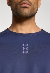 Αθλητική μπλούζα σε ναυτικό μπλε με στρογγυλή λαιμόκοψη, με υφασμάτινη υφή και κάθετο μοτίβο από ανοιχτό μωβ λογότυπα.