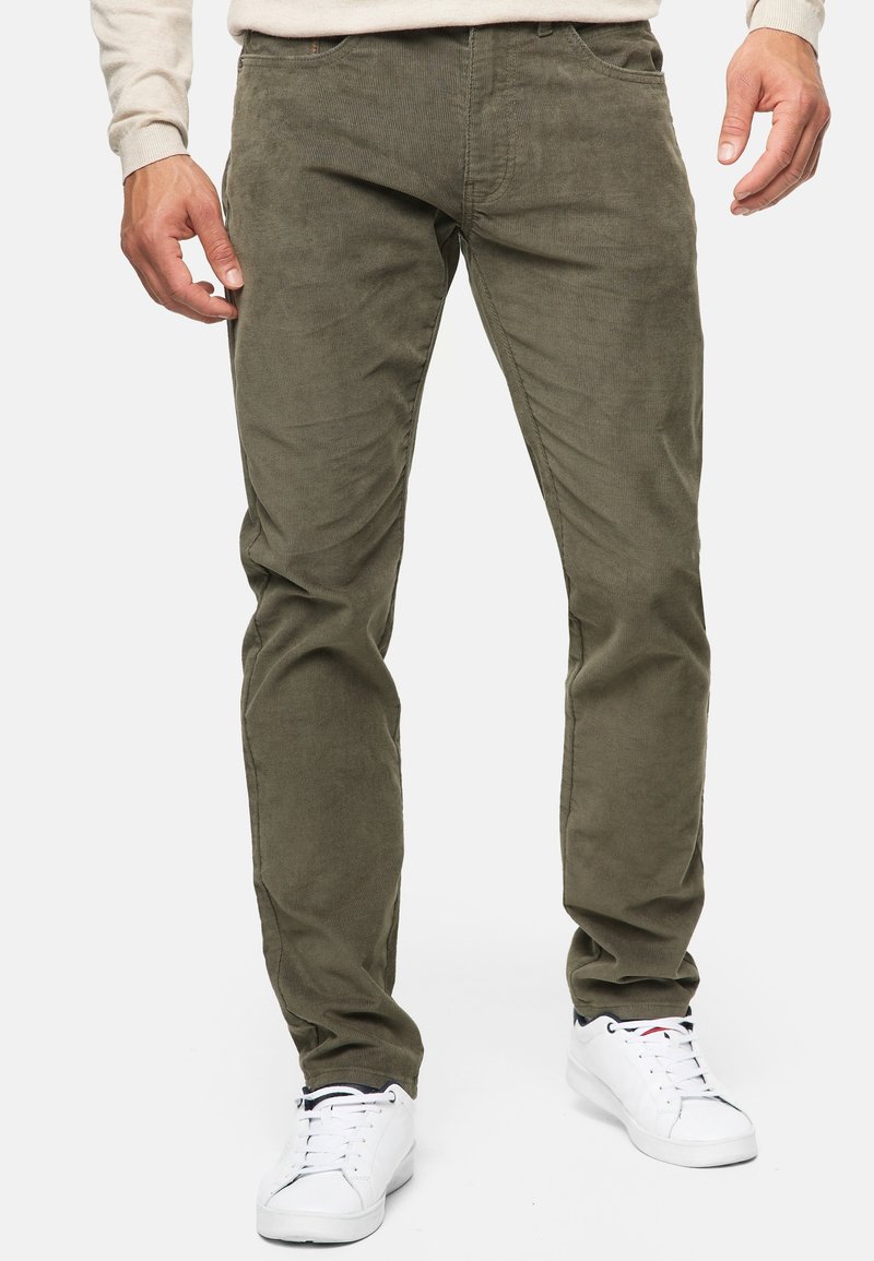 Olivgrüne Cordhosen im Slim Fit mit klassischem Five-Pocket-Design und subtiler Textur. Kombiniert mit weißen Sneakern.