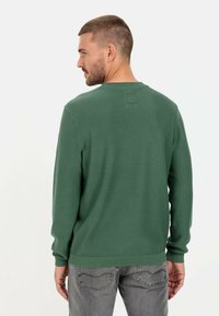 Green textured sweater with long sleeves and a ribbed neckline. Styled with gray jeans, showcasing a casual fit.