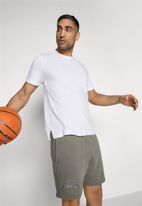 T-shirt branca de gola redonda combinada com calções cinzentos com o logótipo "Los Angeles Lakers" bordado. O conjunto é casual e desportivo.