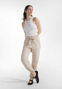 Hvid ribbet croppet top og beige joggers med elastik i taljen, med snøre. Modellen har sorte flade sko med ankelbånd. Glatte teksturer.