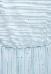 Υφασμα σε ανοιχτό γαλάζιο χρώμα με πιέτες και οριζόντιες ραβδώσεις, καθώς και μικρές ασημένιες κουκκίδες ομοιόμορφα κατανεμημένες στην επιφάνεια.