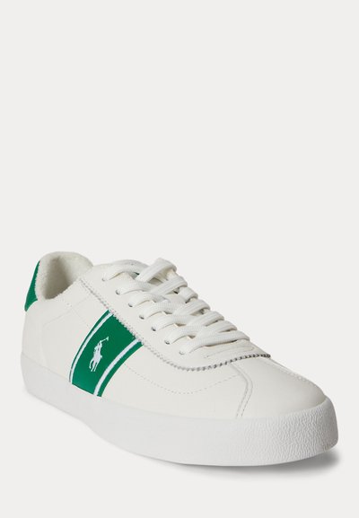 Baskets blanches basses avec bande latérale verte et logo, lacets blancs, et semelle blanche texturée, vue avant en angle sur fond uni.