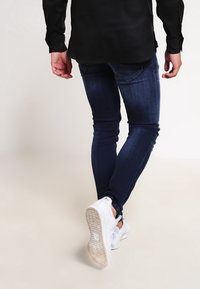 Jeans ajustados de color azul oscuro con una textura suave, combinados con zapatillas blancas que tienen una suela texturada y un diseño minimalista.