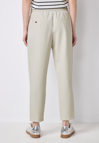 Lichtbeige broek met een elastische tailleband, twee achterzakken en een slim-fit ontwerp. Draag met metallic zilveren sneakers.