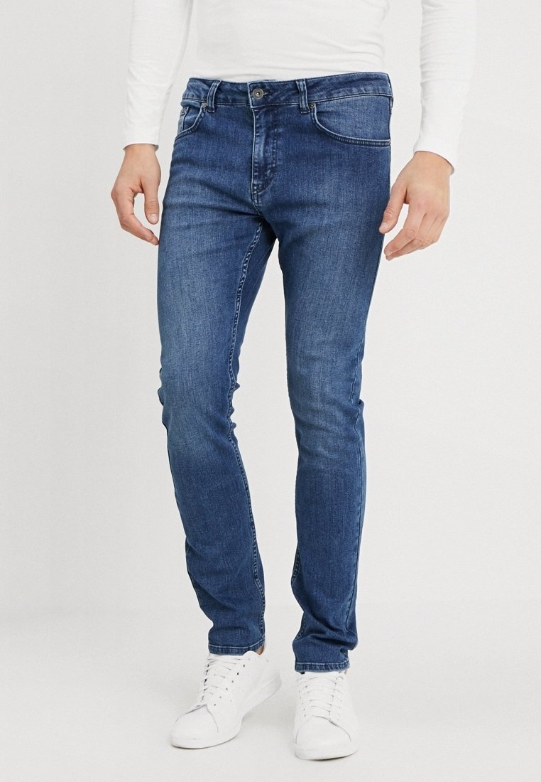Blå denimjeans med slim fit och lätt urtvättning, med knappstängning och frampoketar. Bärs med vita sneakers.
