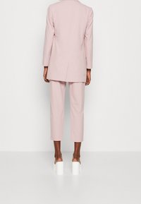 Lichtroze, op maat gemaakte blazer en bijpassende cropped broek, met een gestructureerd ontwerp, gladde stof en witte sandalen met blokhak.