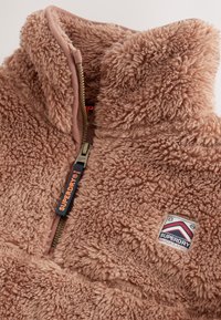 Giacca in pile teddy morbida marrone con collo alto, zip frontale con tiretto "Superdry" e toppa con logo "Superdry Mountain Sport".