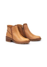 Bottines en cuir tan avec une fermeture éclair sur le côté et des coutures décoratives sur le flanc extérieur. Talon bloc et semelle en caoutchouc texturé pour une meilleure adhérence.