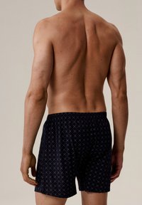 Męskie granatowe bokserki w diamentowy wzór, z elastycznym pasem i luźnym krojem, pokazane z tyłu na nagiej torsie.