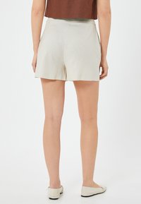 Shorts beige clair avec une texture lisse, une coupe mi-haute et droite, dotés d'un style minimaliste et sans fermetures visibles.