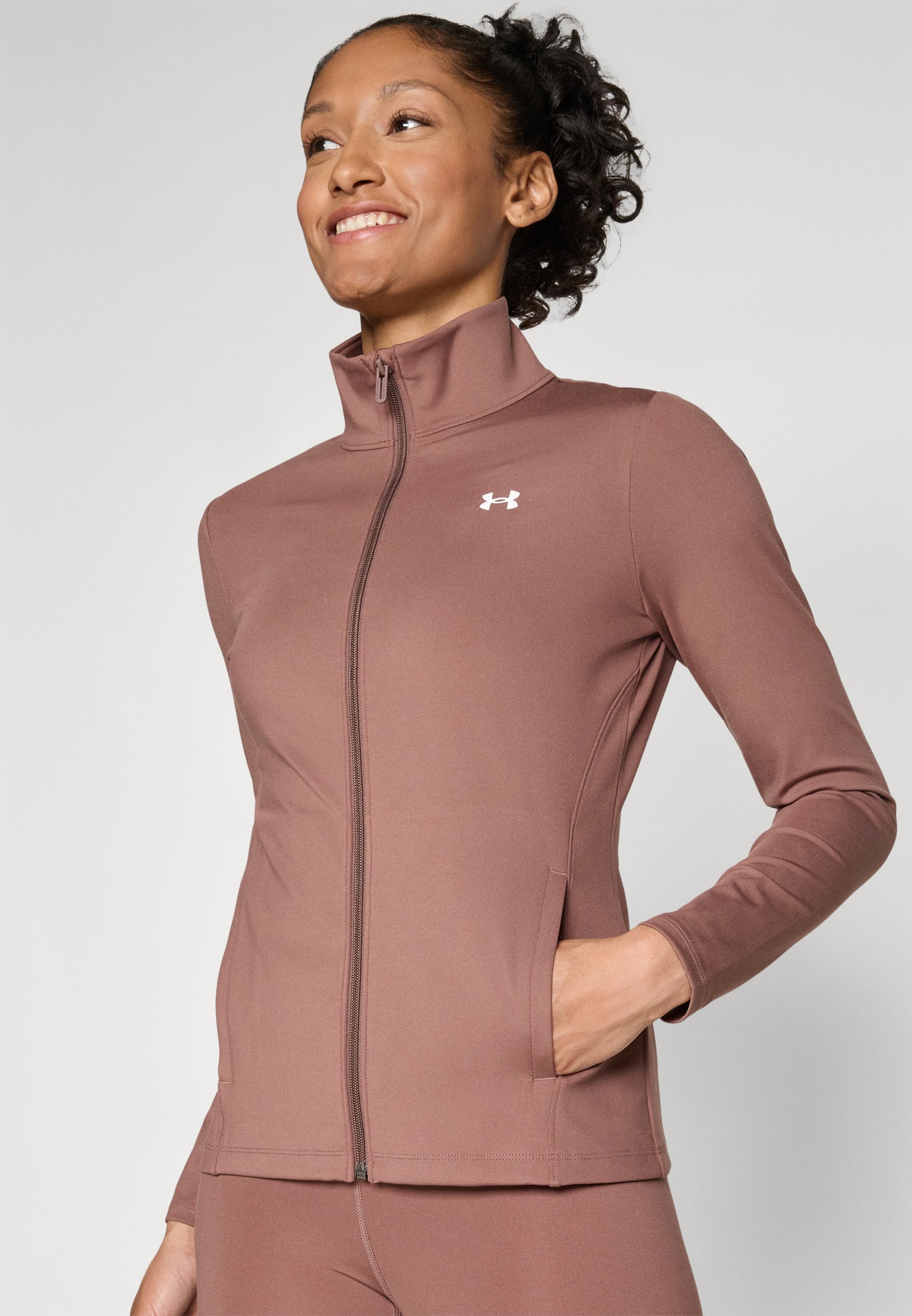 Brown zip-up jacket made of smooth fabric with a high collar, side pockets, and a white logo on the upper left chest.