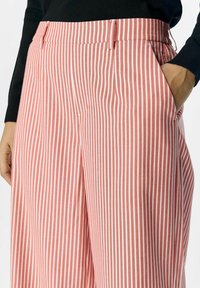 Pantaloni a righe rosse e bianche con una vestibilità comoda, dotati di tasche laterali e una vita frontale piatta. Tessuto dal tocco liscio.