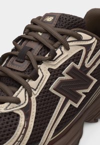 Baskets New Balance marron et beige avec tige en mesh, lacets croisés et logo brodé sur le côté et la languette.