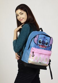 Mochila de tela azul con un gráfico del personaje Stitch, un bolsillo con cremallera rosa con gotas color crema y acentos negros.