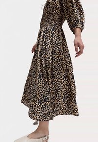 Robe à imprimé léopard avec un corsage smocké, de longues manches bouffantes et une jupe fluide. Le tissu a une texture lisse et légère.