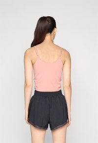 Rosa rosa tettskjorte med justerbare stropper, parret med løse svarte treningsshorts med buet kant og elastisk midje.