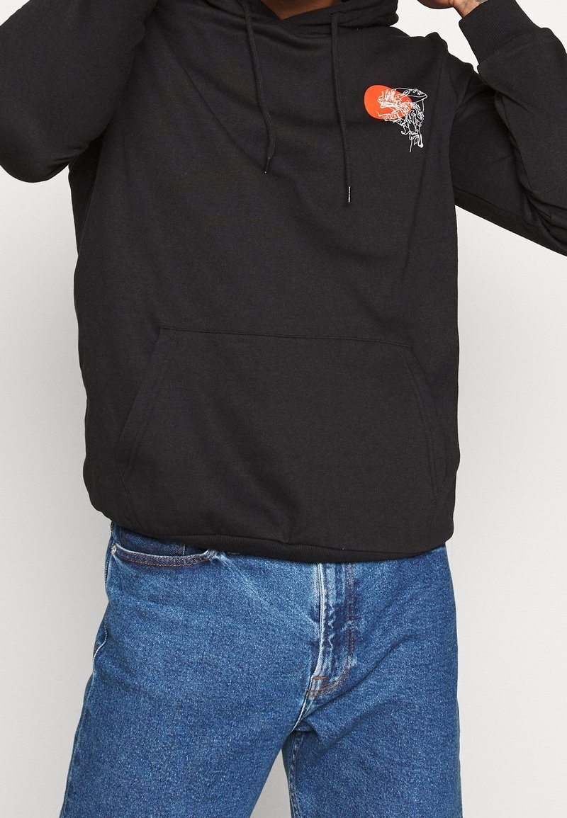 Sudadera con capucha negra y bolsillo frontal, que presenta un círculo rojo y un diseño gráfico. Tejido de mezcla de algodón con un acabado texturizado.