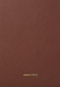 Couverture en cuir marron texturé avec "ANNA FIELD" embossé en lettres dorées en bas. Pas d'autres embellissements ou motifs présents.