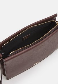 Brązowa skórzana kopertówka o teksturowanej powierzchni, z zapięciem na suwak i czarnym wnętrzem. Posiada złoty zamek i minimalistyczny design.