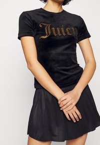 Svart velour T-shirt med korta ärmar och rund halsringning, med en glittrande "Juicy"-design i guldaccent.