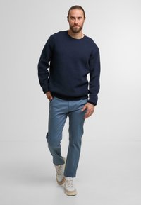 Maglione in cotone blu navy a girocollo abbinato a pantaloni azzurri e sneakers bianche. Il maglione presenta orli e polsini a costine.