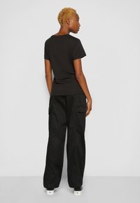 T-shirt nera in cotone a maniche corte, abbinata a pantaloni cargo neri con tasche laterali. L'outfit presenta un design semplice e casual.