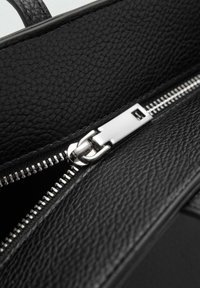 Vnitřek černé kožené tašky se stříbrným zipem. Texturovaný materiál, elegantní design a viditelný funkční mechanismus zipu.