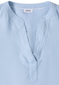 Blouse en lin bleu clair avec un col rond et une encolure en V, présentant des coutures visibles et une étiquette de la marque "CECIL" à l'intérieur du col.