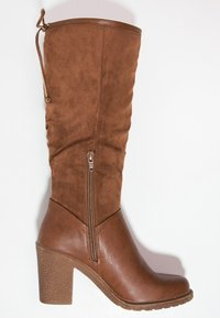 Botte montante marron en suédine synthétique avec une fermeture éclair latérale, un talon épais texturé et un design plissé sur la tige. Accent en cuir lisse à la base.