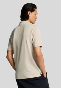 Polo beige realizzato in morbido cotone, maniche corte e colletto classico. Dettagli di cucitura discreti al colletto e all'orlo.