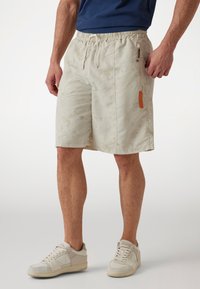 Beige shorts with a subtle pattern, elastic waistband, drawstring, and side zip pocket featuring an orange logo detail. Casual, lightweight design.